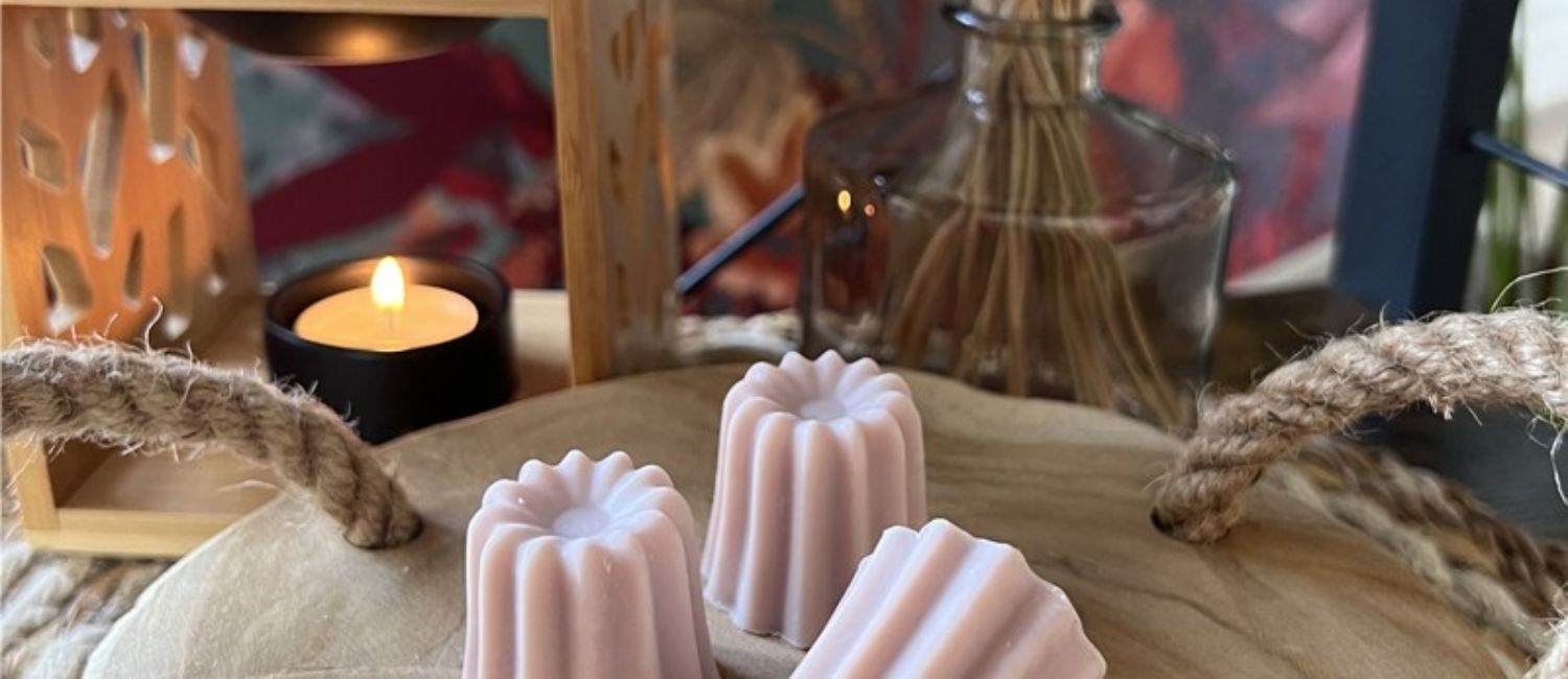 Trois fondants parfumés à la rose, posés sur une table en bois, avec une bougie en arrière plan