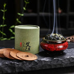 Une boîte d'encens à l'armoise avec plusieurs spirale et un brûloir fumant posés sur une pierre noire