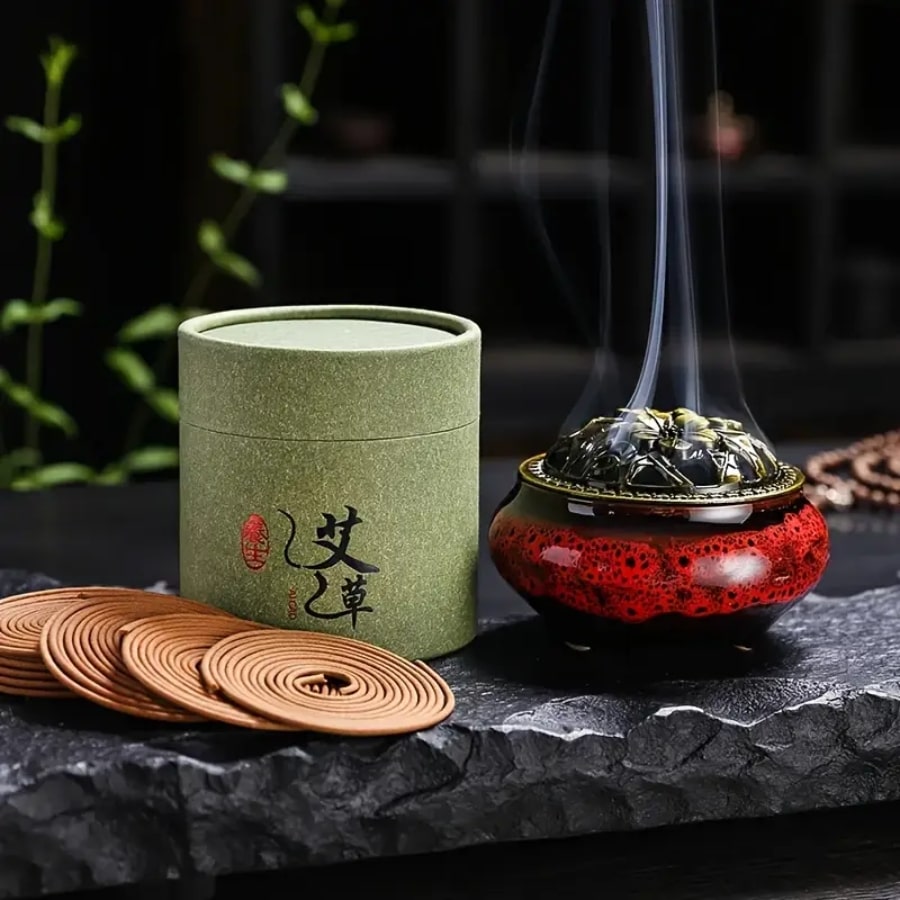 Une boîte d'encens à l'armoise avec plusieurs spirale et un brûloir fumant posés sur une pierre noire