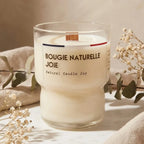 Bougie naturelle ivoire à mèche en bois, entourée de fleurs séchées et linges, sur surface en marbre