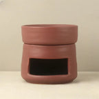 Un brûleur d'huiles essentielles en céramique de couleur bordeaux sur un fond beige