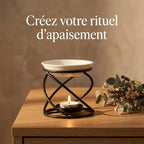 Brûleur d'arômes design courbe métal noir et céramique blanche sur bureau avec bougie et fleurs séchées