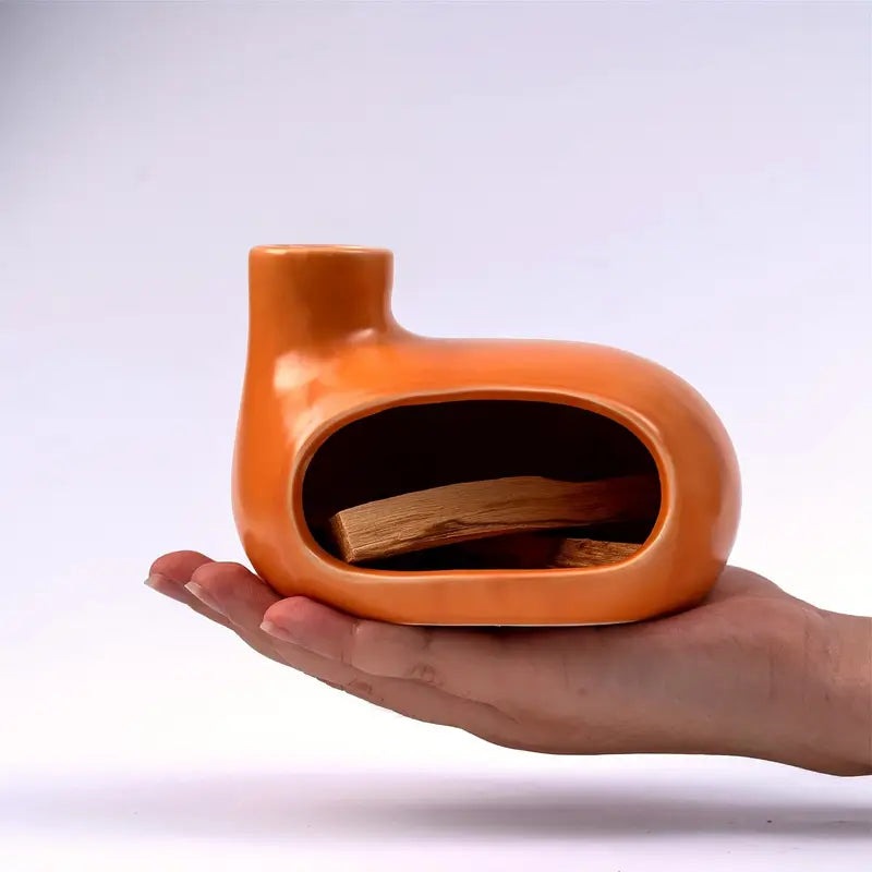 Un brûleur d'Encens & Palo Santo en Céramique modèle Petite maison orange tenu dans la paume de la main