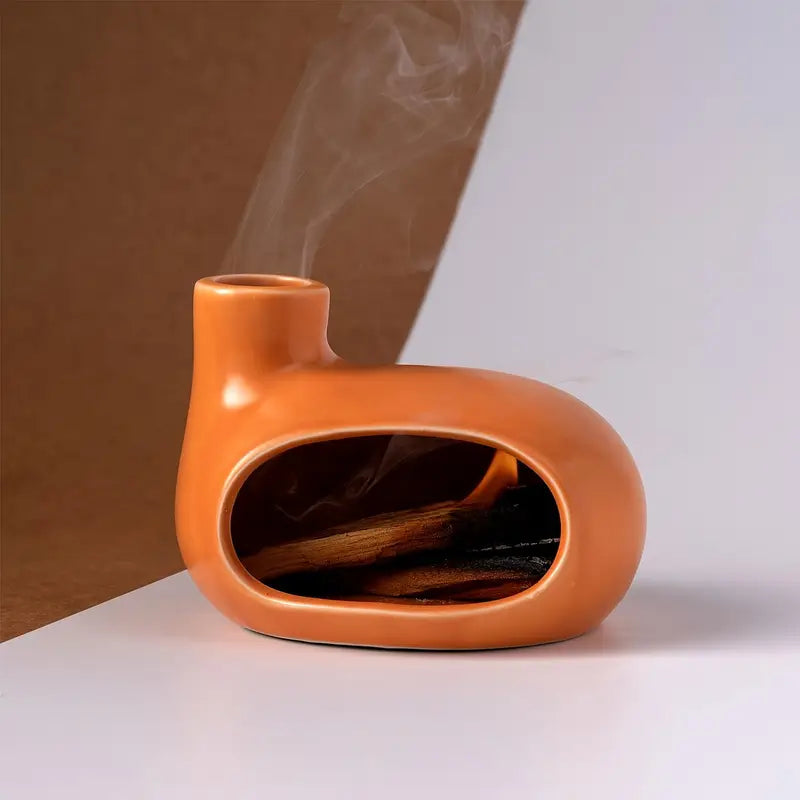 Un Brûleur d'Encens & Palo Santo en Céramique modèle Petite maison orange posé sur une surface plane blanche