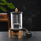 Un Brûleur d’encens à reflux en céramique & verre avec support bois posé sur une table en marbre noir