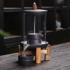 Un Brûleur d’encens à reflux en céramique & verre avec support bois posé sur une table en bois noir