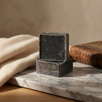 Carrés d'Ambre Musc Noir ByBazz 50g empilés sur marbre, ambiance luxe minimaliste