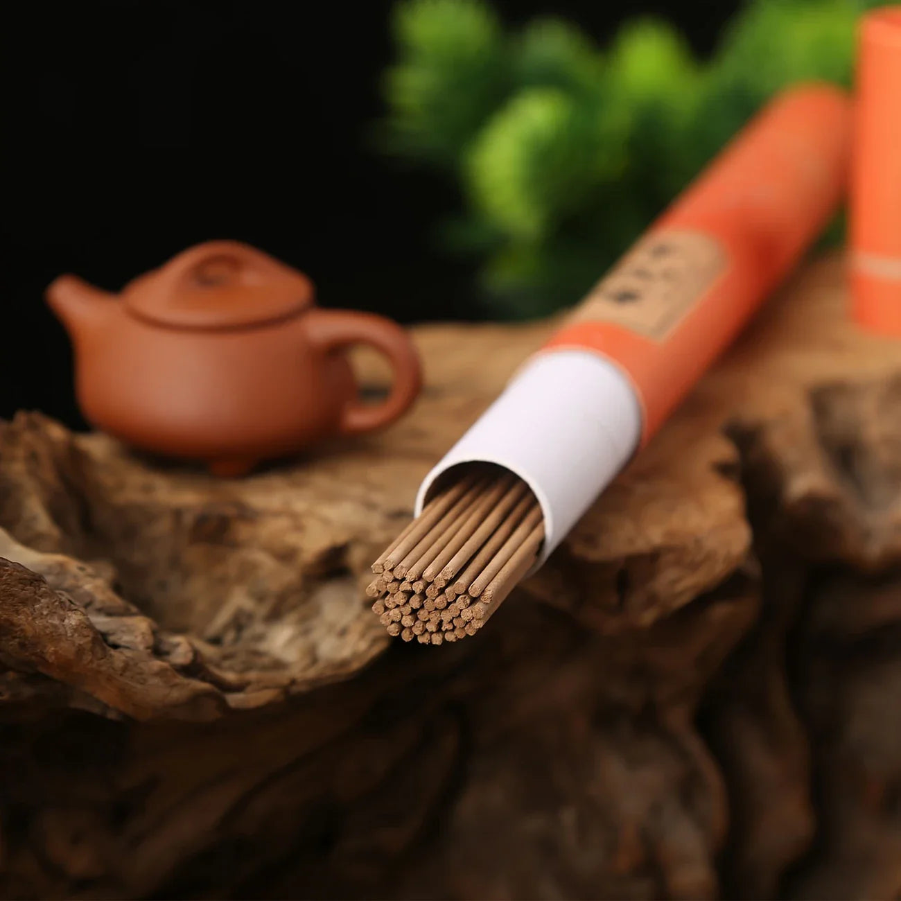 Des batons d'encens posés sur une table en bois à côté d'une teillère en terre cuite