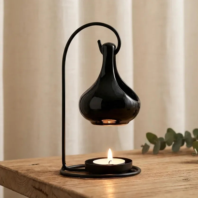 Diffuseur suspendu noir à bougie avec flamme allumée sur surface bois, ambiance aromathérapie spa