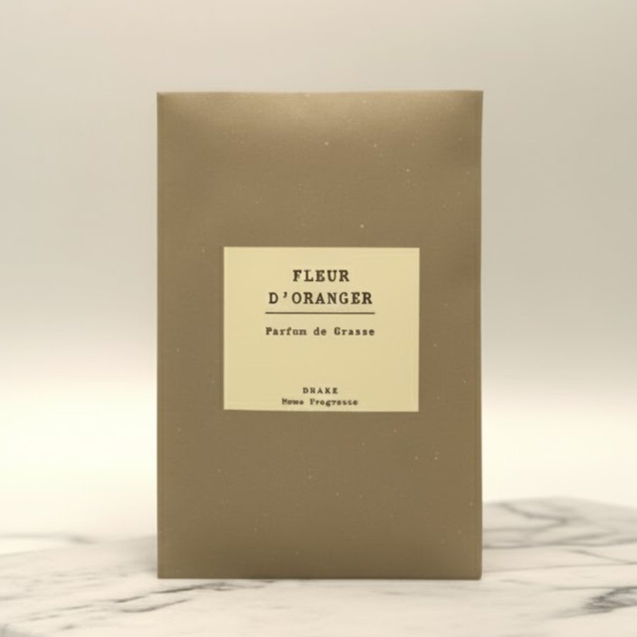 Une enveloppe parfumée à la fleur d'oranger de la marque Drake sur fond beige, posée sur un plateau en marbre