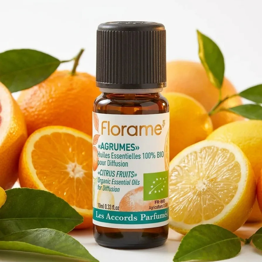 Huile essentielle agrumes bio Florame 10ml entourée d'agrumes frais et feuilles vertes