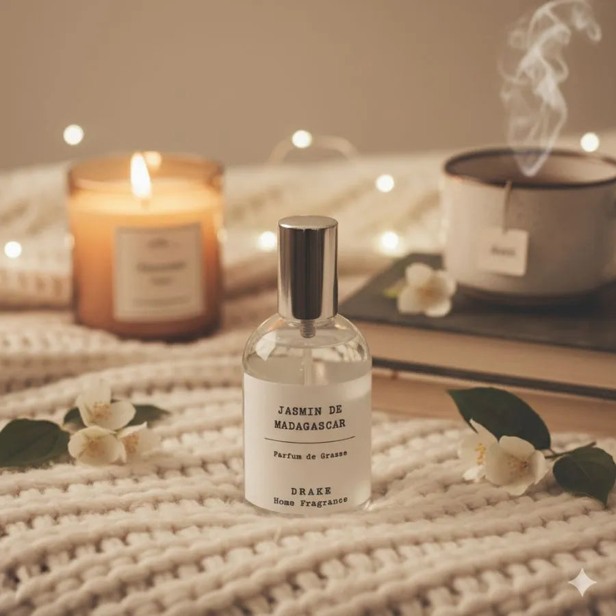 Un spray d'ambiance jasmin de madagascar de la marque Drake posé sur un plaid en laine avec des bougies et une tasse de thé